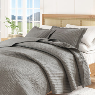 Gray quilted cover on a bed with pillows in a bright bedroom.